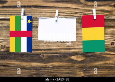 Hanging flags of Central African Republic and Guinea attached to rope with clothes pins with copy space on white note paper on wooden background.Diplo Stock Photo