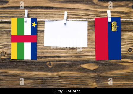 Hanging flags of Central African Republic and Liechtenstein attached to rope with clothes pins with copy space on white note paper on wooden backgroun Stock Photo