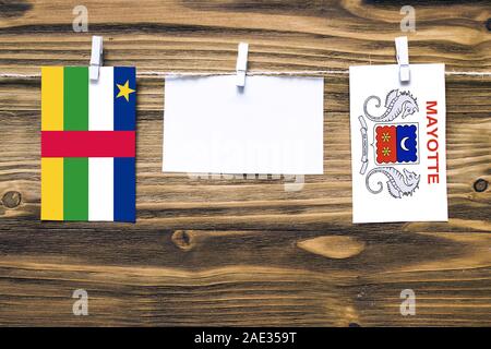 Hanging flags of Central African Republic and Mayotte attached to rope with clothes pins with copy space on white note paper on wooden background.Dipl Stock Photo