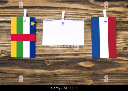 Hanging flags of Central African Republic and Netherlands attached to rope with clothes pins with copy space on white note paper on wooden background. Stock Photo