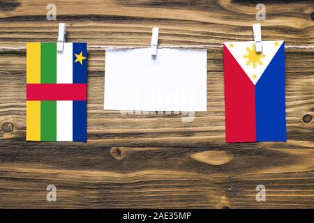 Hanging flags of Central African Republic and Philippines attached to rope with clothes pins with copy space on white note paper on wooden background. Stock Photo