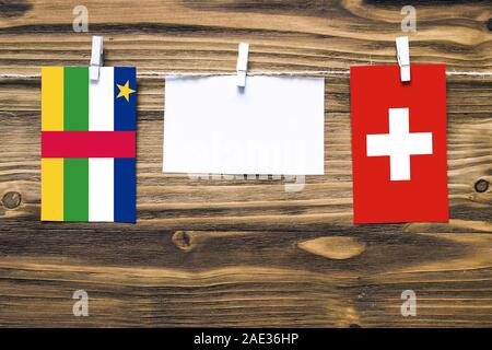 Hanging flags of Central African Republic and Switzerland attached to rope with clothes pins with copy space on white note paper on wooden background. Stock Photo