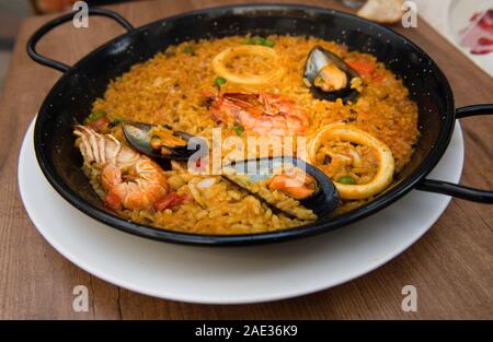 Paella isolated on natural dark background, traditional Spanish food, seafood paella in the fry pan with mussels, king prawns, langoustine and squids. Stock Photo