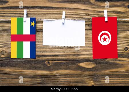 Hanging flags of Central African Republic and Tunisia attached to rope with clothes pins with copy space on white note paper on wooden background.Dipl Stock Photo