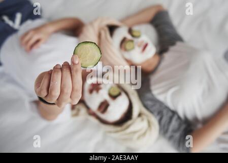Detailed view. Girl holds cucumber ring in the hand. Lying on the white bed. Conception of skin care Stock Photo