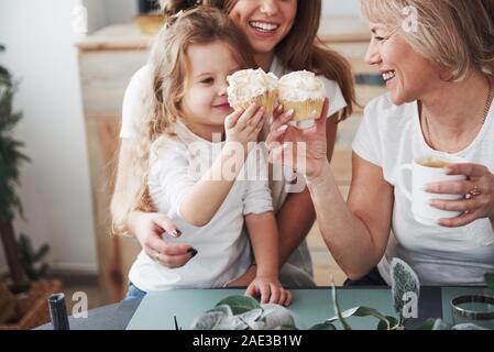 Making a toast with little cakes. Mother, grandmother and daughter having good time in the kitchen Stock Photo