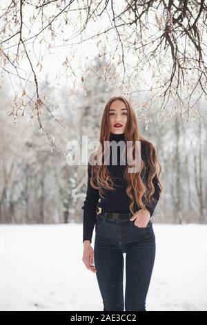 Young model. Pretty girl with long hair and in black blouse is in the winter forest Stock Photo