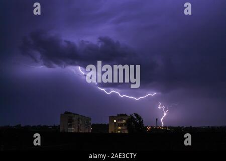 Lightning in big cloud over night city. Black stormy backdrop. Thunderstorm weather. Sky clouds. Dark dramatic scene. Night thunder-storm. Stock Photo