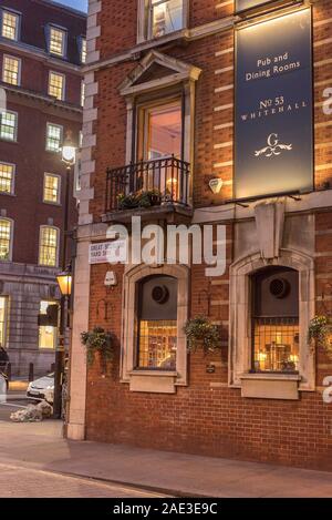 Exterior of The Clarence Pub, 53 Whitehall, central London, UK showing street sign for Great Scotland Yard, SW1 - lit up at night. Stock Photo