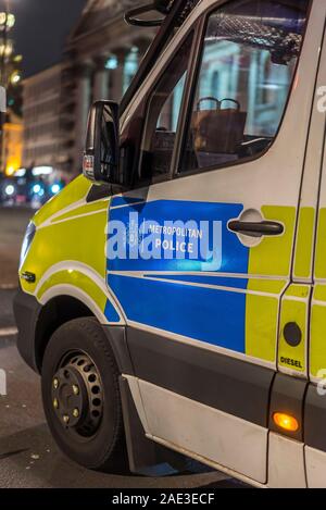 Night time close up of passenger side door of police van showing wording Metropolitan Police, illuminated city buildings in background. Stock Photo