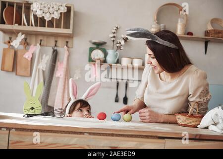 Red, blue and yellow colored eggs. Mother and daughter in bunny ears at easter time have some fun in the kitchen at daytime Stock Photo