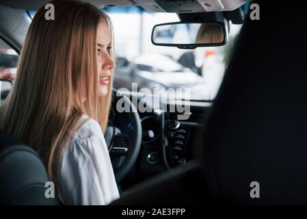 View from behind of the seats. Beautiful blonde girl sitting in the new car with modern black interior Stock Photo