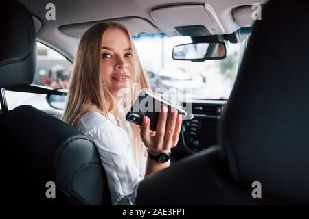 With a phone in hand. Beautiful blonde girl sitting in the new car with modern black interior Stock Photo