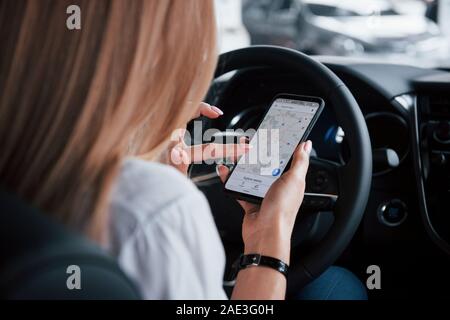Watching the map by using smartphone. Beautiful blonde girl sitting in the new car with modern black interior Stock Photo