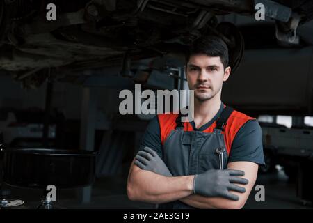 Portrait of serious worker in uniform that stands in his workshop with wrench in hand Stock Photo