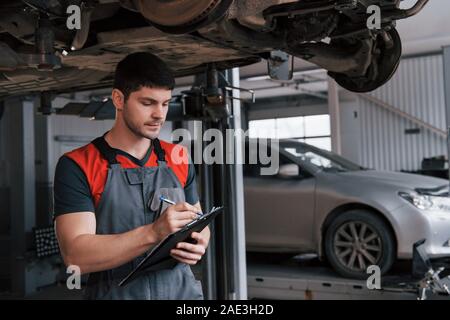 Making report. Man at the workshop in uniform using notepad for his job for fixing broken car Stock Photo