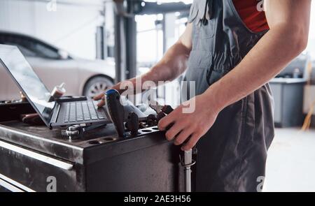 Working hands. Man indoors in uniform using laptop for his job for fixing broken car Stock Photo