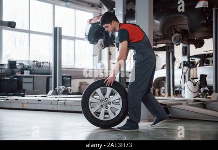 Photo in motion. Mechanic holding a tire at the repair garage. Replacement of winter and summer tires Stock Photo