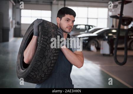 European appearance. Mechanic holding a tire at the repair garage. Replacement of winter and summer tires Stock Photo