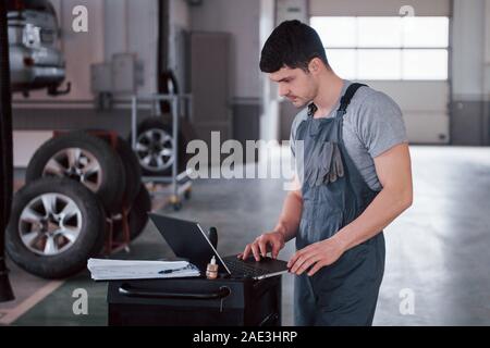 Tires lying on the special stands. Worker stands indoors in uniform does reports, calculations and looking at the plans Stock Photo
