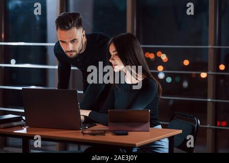 Using modern devices. Team of young business people works on their project at night time in the office Stock Photo