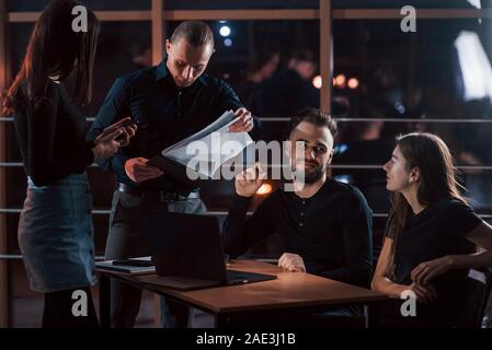Holding notepad with documents. Team of young business people works on their project at night time in the office Stock Photo
