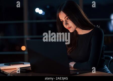 Different digital devices on the table. Attractive brunette businesswoman works alone in the office at nightime Stock Photo
