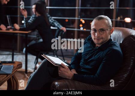 Elegant man in eyewear. Team of young business people works on their project at night time in the office Stock Photo