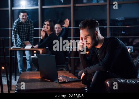 Trying to distract from the job friend who is overworking. Team of young business people works on their project at night time in the office Stock Photo