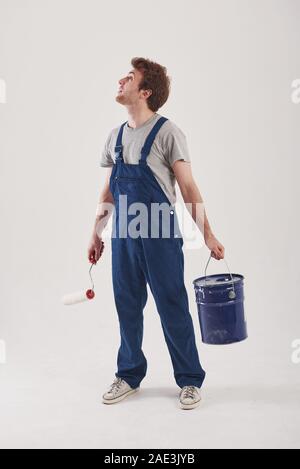 Planning what to paint first. Man in blue uniform stands against white background in the studio Stock Photo