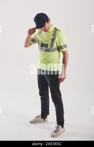 Hiding face behind the hat. Policeman in green uniform stands against white background in the studio Stock Photo