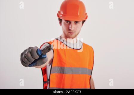 Metal instrument ready for the work. Man in orange colored uniform stands against white background in the studio Stock Photo