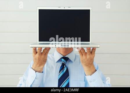 Unrecognizable businessman holding laptop computer in front of his head with the blank screen replacing his face Stock Photo