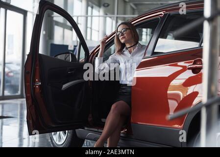 Opening the door. Woman in eyewear, black skirt and white shirt sits in the red automobile Stock Photo