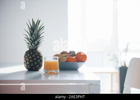Pineapple, bananas, oranges and glass with fresh juice on the table Stock Photo