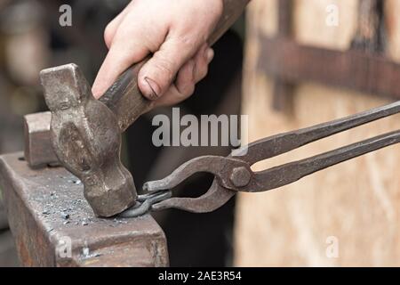 The blacksmith makes an iron loop with a hammer and tongs, forging on the anvil. Stock Photo