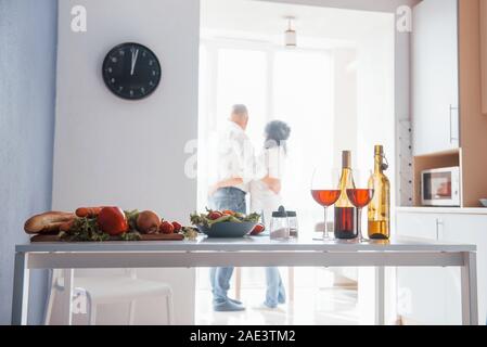 Waiting for the right time and looking through the window. Senior man and his wife in white shirt have romantic dinner on the kitchen Stock Photo