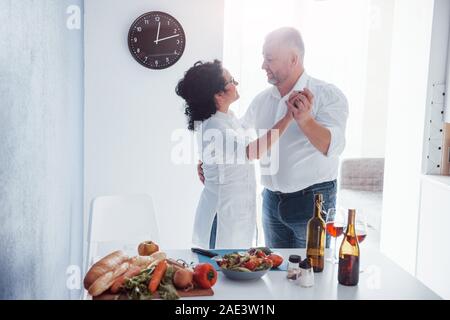 Romantic dinner. Senior man and his wife in white shirt on the kitchen Stock Photo