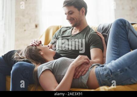 Two people having nice day. Happy couple relaxing on the yellow sofa in the living room of their new house Stock Photo