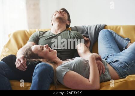 Nice joke. Happy couple relaxing on the yellow sofa in the living room of their new house Stock Photo