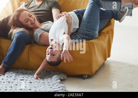 Upside down. Happy family have fun on the yellow sofa in the living room of their new house Stock Photo