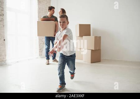 In front of parents. Playful mood from the kid. Family have removal into new house. Unpacking moving boxes Stock Photo