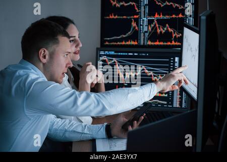 Works at evening. Team of stockbrokers are having a conversation in a office with multiple display screens Stock Photo