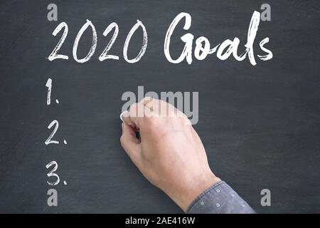Thinking Position of A Young Asian Man while standing directly below blackboard with chalk drawing of new year 2020 Goals Stock Photo