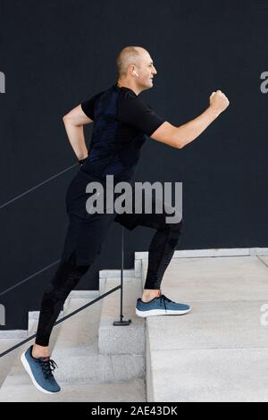 Young tall manly man is active in sports on the street against a black wall background