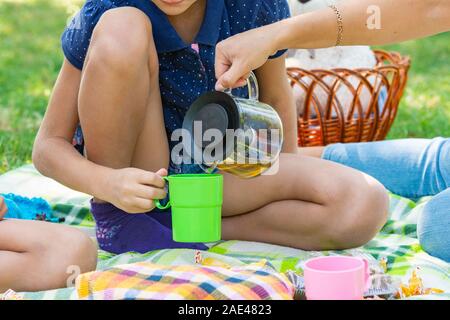 Close-up as a girl pours tea into a teenager's cups on a picnic in the park Stock Photo