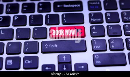 Red key with book now icon on laptop keyboard. The book now button has a text Stock Photo