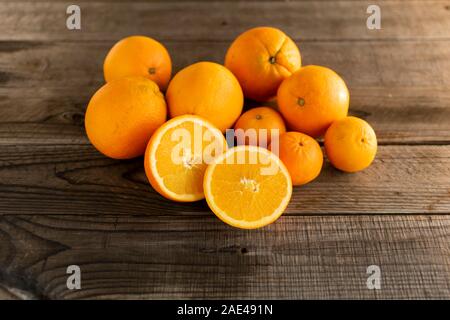 Halved orange with whole oranges and mandarins on a wooden background. Stock Photo
