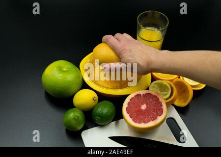Hand squeezes grapefruit in juicer. On black background Stock Photo