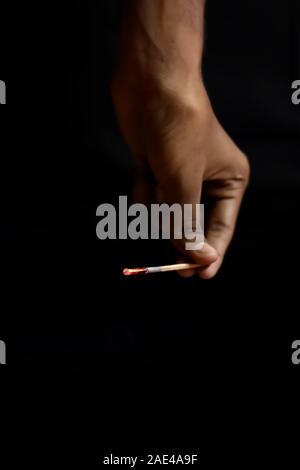 Burnt extinguished match held in hand on black rugged backgrounds Stock Photo